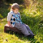 Enfant pensif assis sur une valise dans un champ ensoleillé